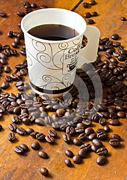 A paper cup of black coffee and coffee beans on table