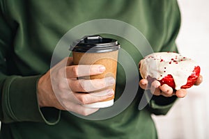 A paper cup of coffee and an appetizing donut in male hands close-up.