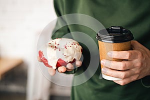 A paper cup of coffee and an appetizing donut in male hands close-up.