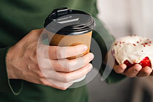 A paper cup of coffee and an appetizing donut in male hands close-up.