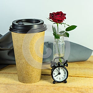 A paper cup with coffee and coffee beans on a wooden table with a red rose. Takeaway coffee in a thermocup, a place to copy.