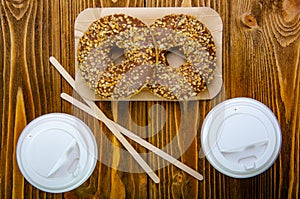 Paper cup for coffee, disposable ecological coffee supplies. Donuts on paper trays. Wooden table.