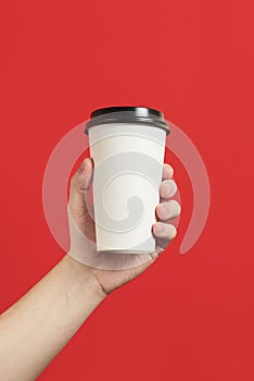 Paper cup of coffee or tea on a red background. Mockup of male hand holding paper cup isolated. Front view mockup of empty