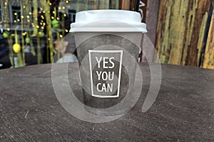 A paper cup for coffee with a white lid is on the table.