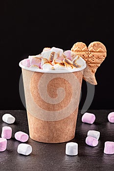 Paper cup with hot drink with marshmallows on dark background. Recycling and eco friendly concept.