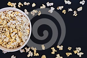 Paper cup with popcorn, and popcorn scattered on a black background, top view, copyspace