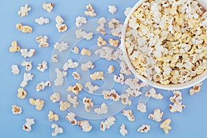 Paper cup with popcorn, and popcorn scattered on a pastel blue background, top view, copyspace