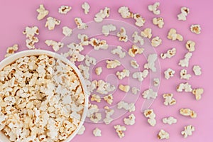 Paper cup with popcorn, and popcorn scattered on a pastel pink background, top view, copyspace