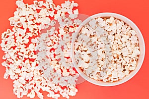 Paper cup with popcorn, and popcorn scattered on a red background, top view, copyspace