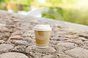 Paper cup on rocky ground outdoors, space for text. Coffee to go