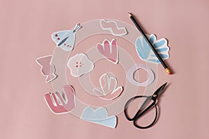 Paper cut abstract shapes, flowers and butterfly. Black old scissors and pencil on pink table background. Kids diy