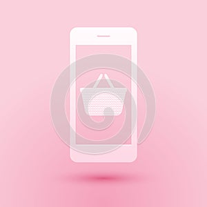 Paper cut Mobile phone and shopping basket icon isolated on pink background. Online buying symbol. Supermarket basket