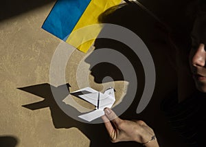 paper dove of peace in female hand, origami, contrast shadows and Ukrainian flag