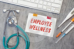 Paper with EMPLOYEE WELLNESS on a table, stethoscope and pills