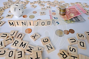 paper euro banknotes, piggy bank, bills on table among euro coins, word Mini job with wood blocks, part-time with low wage concept