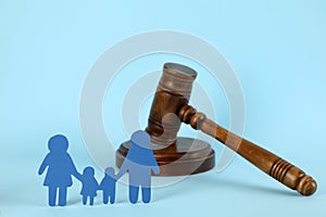 Paper family figure and wooden gavel on light blue background. Child adoption concept