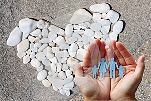 Paper family in hands with a heart of white stones in background welfare concept