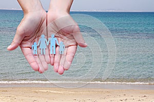 Paper family in hands on sea beach background welfare concept