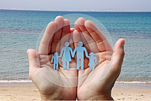 Paper family in hands on sea beach background welfare concept