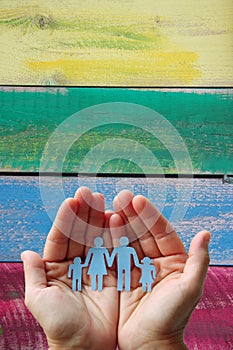 Paper family in hands on wooden coloured background welfare concept