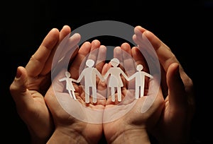 A paper family holding hands, with the protection of a woman`s hands, in turn in the hands of man.