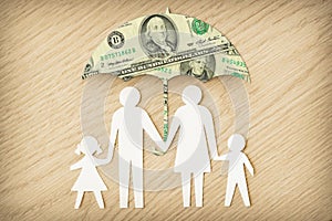 Paper family silhouette with umbrella made of dollar banknotes on wooden background - Concept of family financial protection