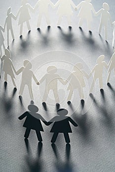 Paper figure of female couple outside of the circle of paper people holding hands on gray surface. Bulling, minorities