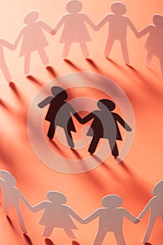 Paper figure of female couple surrounded by circle of paper people holding hands on red surface. Bulling, minorities