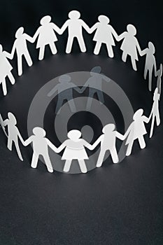 Paper figure of a male couple surrounded by circle of paper people holding hands on dark surface. Bulling, minorities