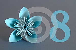 Paper flower from origami with the number eight on a gray background. March 8, International Women's Day.