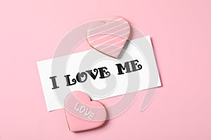 Paper with handwritten phrase I Love Me and heart shaped cookies on pink background, flat lay