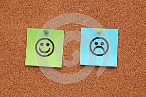 Paper with happy and sad faces on corkboard