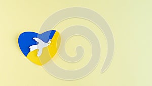 Paper heart with Ukrainian flag colors on yellow background and white dove of peace with olive branch