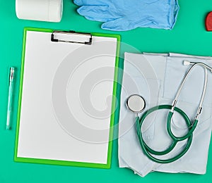 paper holder with empty white sheets, medical stethoscope, pills on a green background