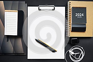 Paper holder next to folders, notepads, pens, calendar, wristwatch and wired headphones