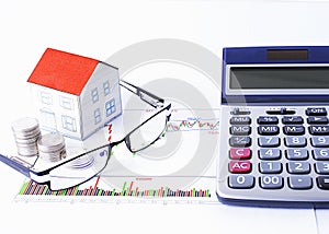 Paper house with coins and eyeglasses and calculator on chart
