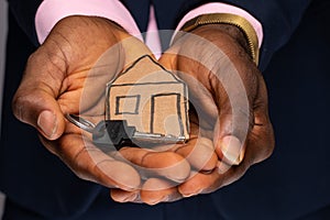 a paper house and key in the palm of a black person& x27;s hand