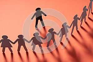 Paper human figure standing in front of paper people holding hands on red surface. Bulling, segregation, conflict photo
