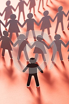 Paper human figure standing in front of paper people holding hands on red surface. Bulling, segregation, conflict photo