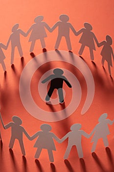 Paper human figure surrounded by circle of paper people holding hands on red surface. Bulling, segregation, conflict photo