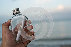 Paper letter in a glass bottle on hand over blurred sea water background