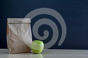 Paper lunch bag on desk with apple