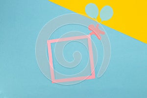 paper man flying paper balloons and holding pink frame as copy space on pastel blue-yellow background