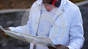 Paper map in hands of troubled man lost in city park. Nervous dissatisfied young unrecognizable African American tourist