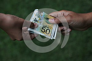 Paper money in hand. Two hands of young woman or man holding 50 AUD Australian dollar on green background. Pay day concept.