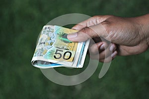 Paper money in hand. Young woman or man holding 50 AUD Australian dollar on green background. Pay day concept. Copy space for text