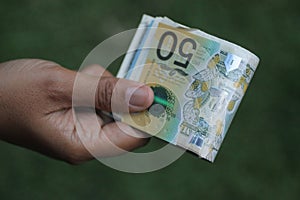 Paper money in hand. Young woman or man holding 50 AUD Australian dollar on green background. Pay day concept. Copy space for text