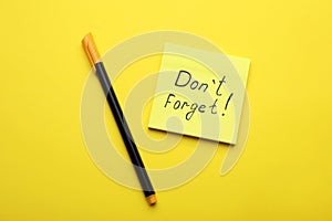 Paper note with phrase Don` t Forget and pen on yellow background, flat lay
