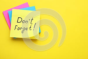 Paper note with phrase Don` t Forget on yellow background, top view. Space for text