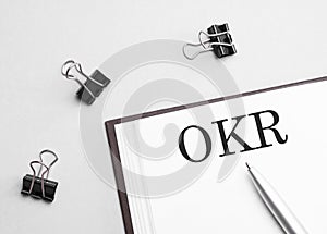 paper note with text okr, pen and office tools, white background. business concept